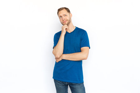 Pensive man thinking and touching chin with hand. Caucasian man looking up, considering ideas, brainstorming, while standing on white background. Imagination, wonder, inspiration conceptの写真素材
