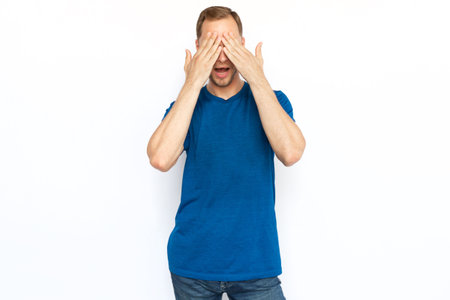 Excited bearded guy covering eyes with hands. Bearded Caucasian man getting nervous, receiving shocked news, while standing on white background. Surprise, happiness conceptの写真素材