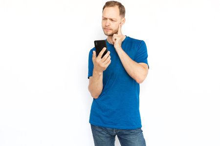 Pensive man thinking and holding mobile phone. Focused bearded man standing on white background, thinking about worried news or what to reply on message. Online communication, cyberspace conceptの写真素材