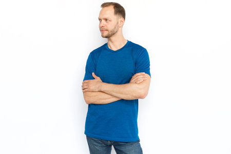 Man standing with folded arms and looking away. Pensive Caucasian man in T-shirt posing for camera while standing on white background. Emotion, confidence, success conceptの写真素材