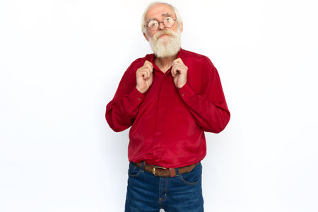 Confident senior man fixing collar. Self-assured Caucasian male model with gray hair and beard in red shirt and glasses looking at camera, smiling with pleased look. Success, self-assurance conceptの写真素材