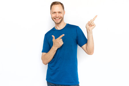 Happy man pointing index finger at copyspace. Cheerful Caucasian man looking at camera, standing on white background, promoting product. Advertisement, promotion conceptの写真素材