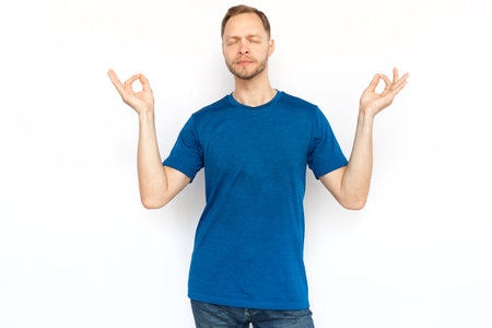 Relaxed man standing and showing zen gesture. Peaceful man standing in lotus position on white background, meditating with closed eyes and breathing. Yoga, relaxation conceptの写真素材