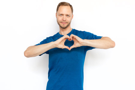 White man showing heart shape with hands at camera. Cheerful man looking at camera, demonstrating tenderness, love, affection while standing on white background. Love, romance conceptの写真素材