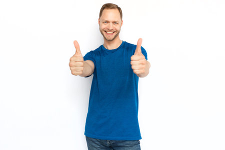 Caucasian man showing thumbs up at camera. Smiling adult man looking at camera, standing on white background, showing approving gesture. Agreement, approval conceptの写真素材