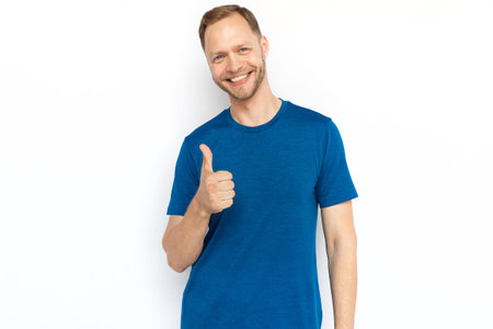 White man showing thumb up at camera and smiling. Happy adult man looking at camera, standing on white background and showing approving gestures. Agreement, approval conceptの写真素材