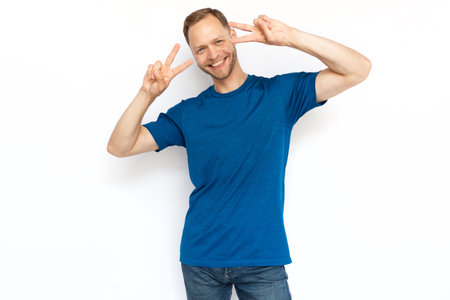 Happy Caucasian man making peace signs and looking at camera. Cheerful bearded guy standing on white background and smiling. Satisfaction, achievement, winning conceptの写真素材