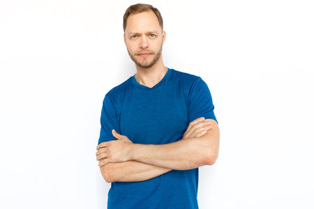 Fair hair Caucasian man standing with folded arms. Portrait of pensive or serious guy in T-shirt looking and posing for camera on white background. Confidence, success, individuality conceptの写真素材
