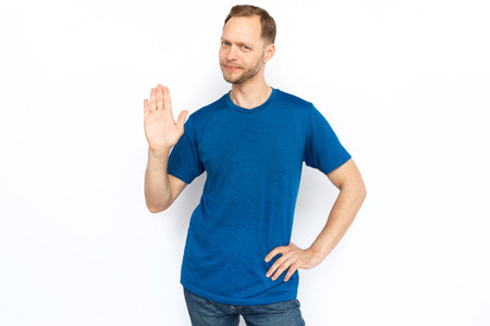 White man showing stop gesture at camera. Guy in T-shirt making rejection sign, declining offer while standing on white background. Protection, safety, defense, control conceptの写真素材
