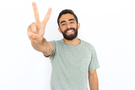 Cheerful man showing peace sign. Young male model making peace gesture and smiling. Portrait, studio shot, peace, victory conceptの写真素材