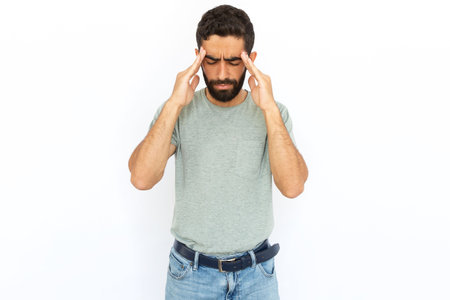Serious man rubbing temples. Young male model experiencing headache. Portrait, studio shot, stress, health conceptの写真素材