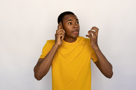 Portrait of irritated young man talking on smartphone. African American guy wearing yellow T-shirt having unpleasant conversation over mobile phone. Unpleasant communication conceptの写真素材