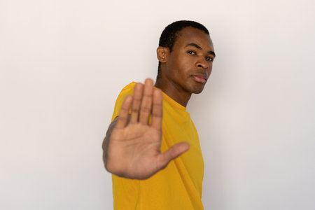 Serious young man showing stop sign. Male African American model with brown eyes and short black...