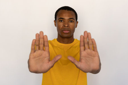 Serious young man showing stop signs. Male African American model with brown eyes and short black haircut in casual clothes showing his palms as stop sign. Warning, forbiddance conceptの写真素材