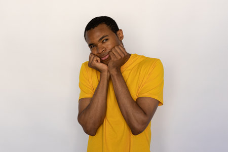 Pensive young man holding his face with hands. Male African American model with brown eyes and short black haircut in yellow T-shirt looking away thinking about life, making decision. Thought conceptの写真素材