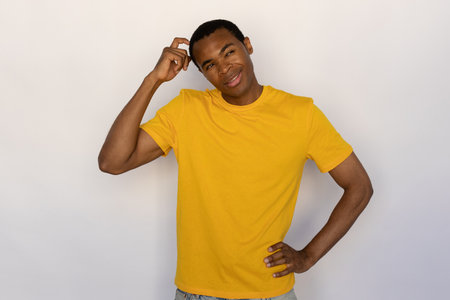 Pensive young man scratching his head thinking. Male African American model with brown eyes and short black haircut in yellow T-shirt looking away making decision. Thought, advertisement conceptの写真素材