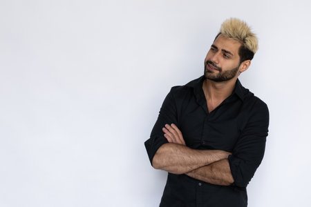 Excited young man looking at copyspace. Male Caucasian model with brown eyes, ombre painted hair and beard in black shirt crossing his hand looking aside. Advertisement conceptの写真素材