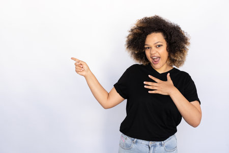 Surprised woman pointing aside. Young female model showing something with hand on chest. Portrait, studio shot, advertising conceptの写真素材