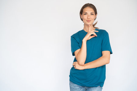 Pleased Caucasian woman leaning on hand. Portrait of graceful young female model with brown hair in blue T-shirt looking at camera, smiling and touching chin with finger. Skincare, happiness conceptの写真素材
