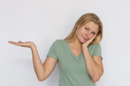 Bored young woman showing ads with palm. Portrait of tired Caucasian female model with fair hair in...