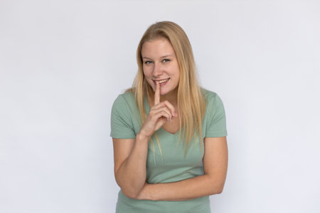 Smiling woman holding finger at lips. Young female model smiling and showing hush gesture. Portrait,...
