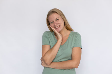 Happy young woman leaning on hand. Portrait of content Caucasian female model with fair hair in green T-shirt looking at camera, smiling, reacting to something cute. Kindness, sympathy conceptの写真素材