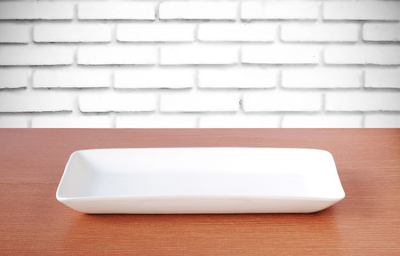 Empty plate on wood table over white brick wall background, template, food and drinksの写真素材