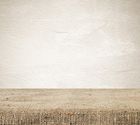 Empty table covered with sackcloth over grunge cement wall  backgroundの写真素材