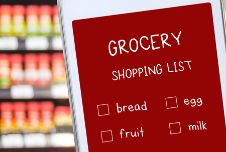 Smart phone with grocery online shopping list on screen over blur product shelves, bussiness and technology conceptの写真素材