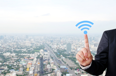 Businessman hand pointing wifi icon over blur city scrape background, internet of things conceptの写真素材