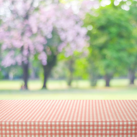 Empty table with pink and beige scott pattern tablecloth over blur park background, food and product...