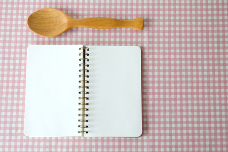Blank note book and wooden spoon on white and pink tablecloth, cook book background, menu, food concept, flat layの写真素材
