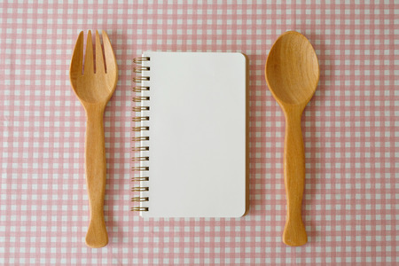 Blank note book and wooden fork, spoon on white and pink tablecloth, cook book background, menu, food concept, flat layの写真素材