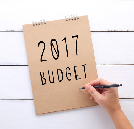 Hand holding pen over 2017 budget notebook on white wood background, business and finance conceptの写真素材