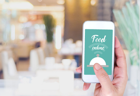 Hand holding smart phone with food online device on screen over blur restaurant background, food online, food delivery conceptの写真素材