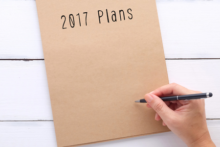 Hand holding pen over blank recycle paper notebook with 2017 plans word background, with copy space for text, sucess in business conceptの写真素材