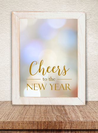 White wooden frame with Cheers to  New Year words over blur bokeh on table and cement wall bacgroundの写真素材