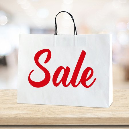 Sale on white shopping bag over blur store background, discount promotion, business conceptの写真素材