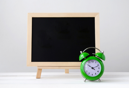 Green alarm clock and empty black board on white table, space for textの写真素材