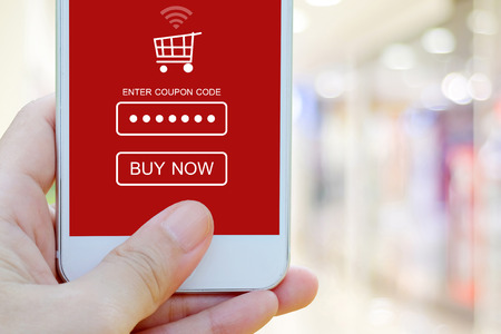 Hand holding smart phone with discount coupon code on screen over blur store background, on line shopping ,business, E-commerce, technology and digital marketing backgroundの写真素材