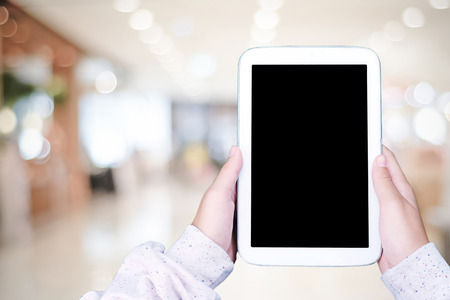 Hand using blank screen tablet over blur store with bokeh background, mock up, business and...
