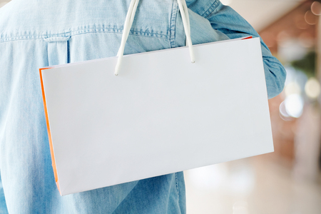 Hand holding white shopping bag on blur store background with copy space for text, template, business conceptの写真素材