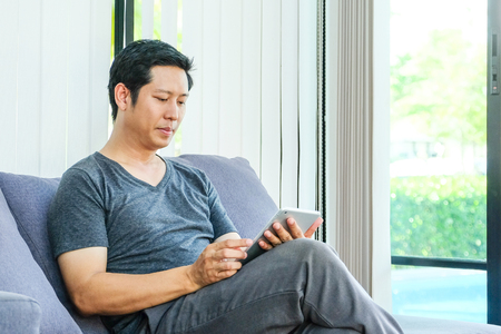 Man using tablet sitting on sofa at home, technology and lifestyle conceptの写真素材