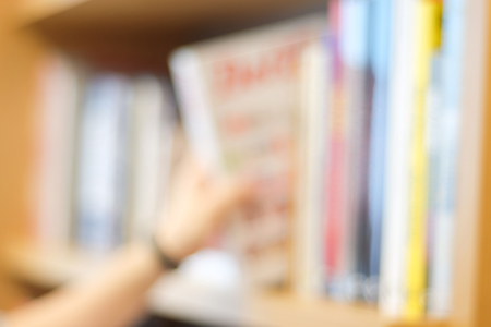 Blurred background : Blur hand picking book from bookshelf at library, education concept backgroundの写真素材