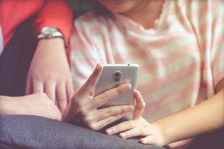 Woman hand using smart phone while sitting on sofa with her friend in casual lifestyle, vintage tone background, woman on phone conceptの写真素材