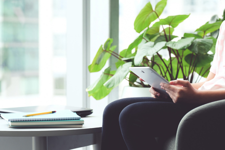 Woman student using tablet while sitting on sofa by window with copy space for text, online education concept backgroundの写真素材