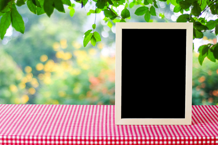 Blank chalkboard standing red check tablecloth over blur tree background, space for text, mock up, product display montageの写真素材