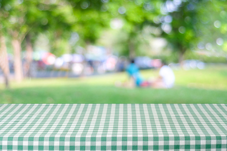 Empty table with green tablecloth over blur park with people and bokeh background, food and product display montageの写真素材