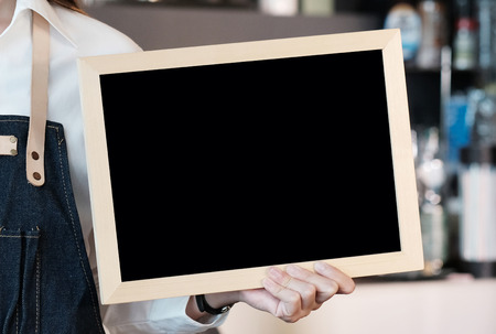 Hand holding blank chalkboard in font of cafe counter background, menu board, food and drinksの写真素材