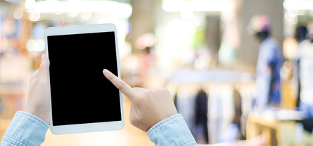 Hand using tablet with blank screen for mock up over blur store background, banner, business and...